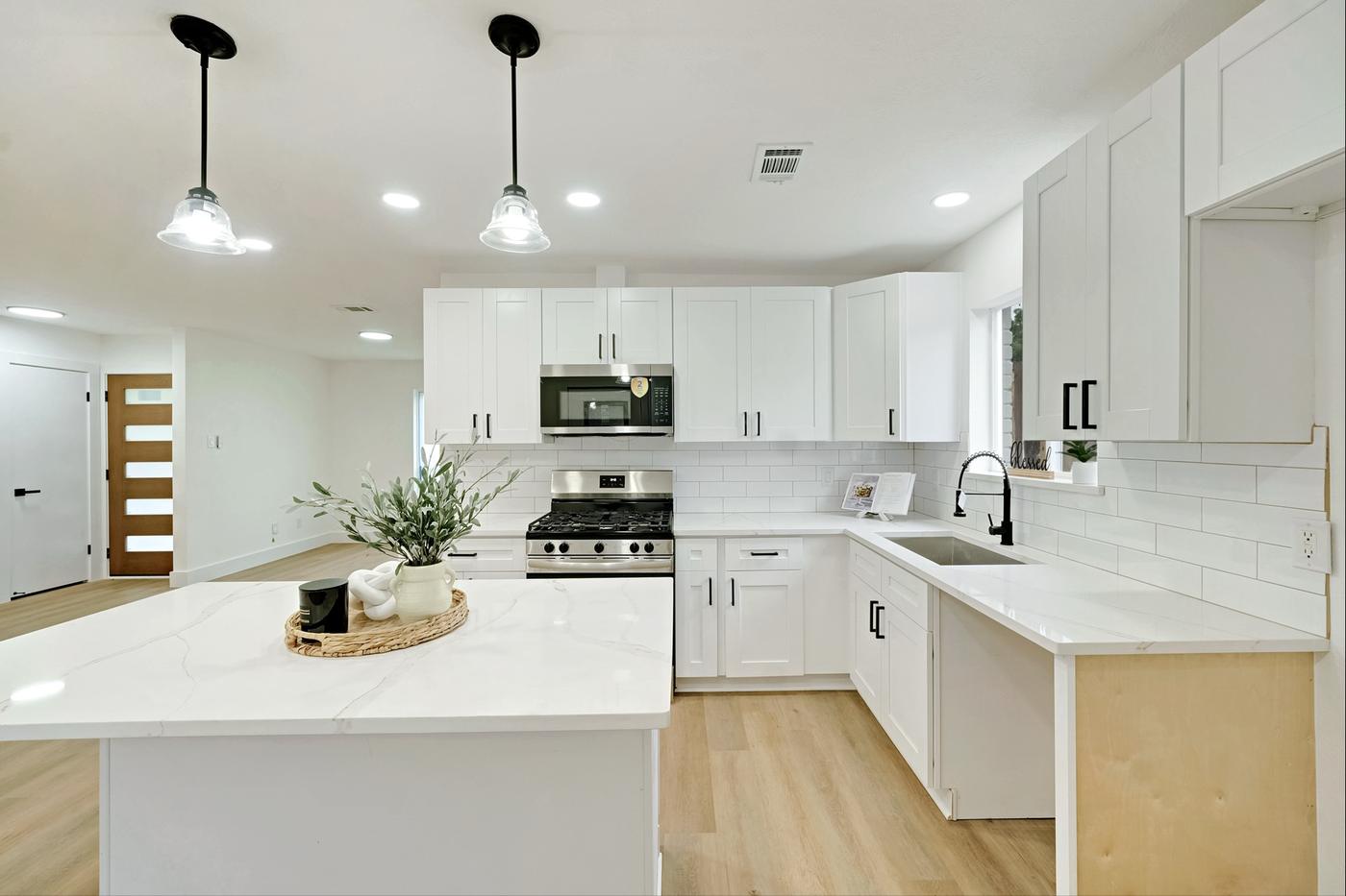 Bright kitchen with black pendant lights over a white island and marble backsplash