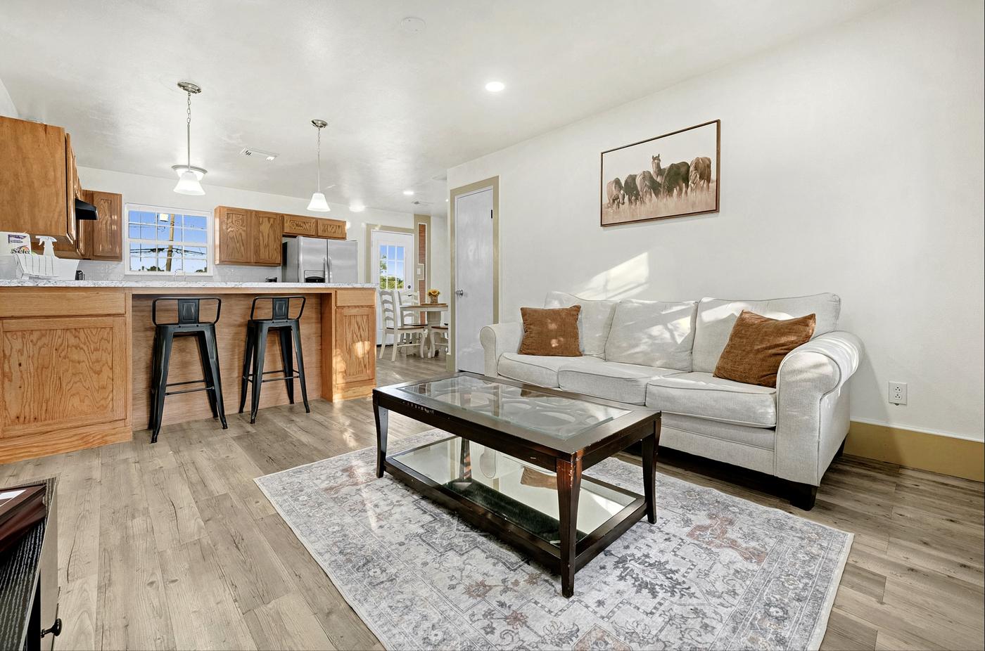 Living room with white sofas and a glass coffee table open to a wood kitchen